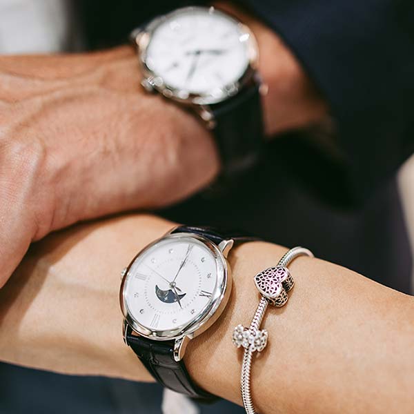Schönes Paar genießt den Einkauf im modernen Juweliergeschäft. Nahaufnahme einer menschlichen Hand, die eine teure Uhr hält.