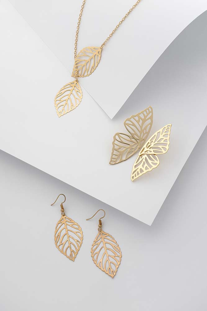 Von der Natur inspiriertes Schmuckset – Blätterförmige Ohrringe und Halskette mit schmetterlingsförmigen Ohrringen auf weißem gefaltetem Papier